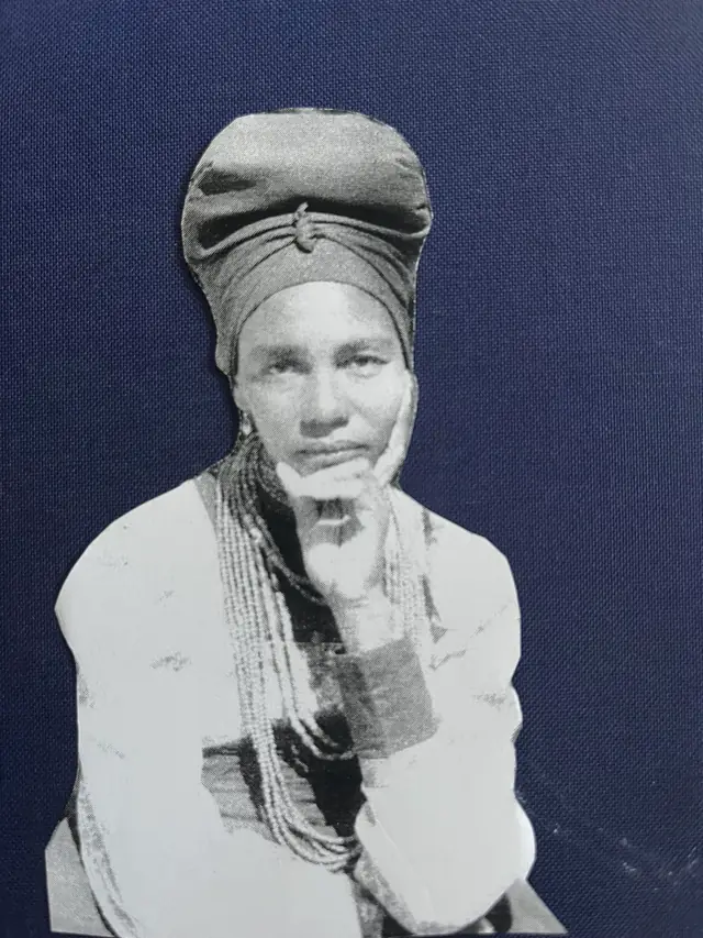 Adelheid Mbwaondjou wearing a headwrap, with one hand against her cheek.
